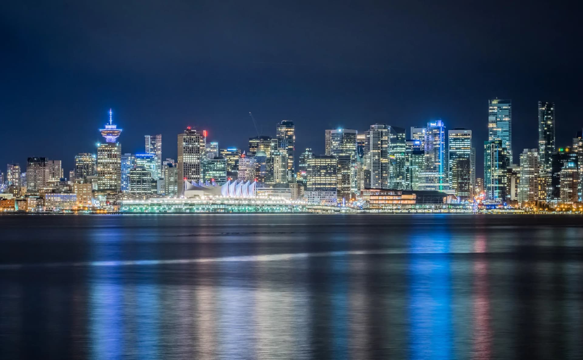 Downtown Vancouver skyline lit up at night across Burrard Inlet, with Canada Place and Harbour Centre reflected in the water