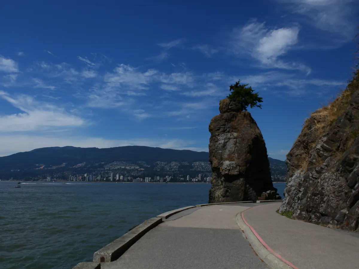 Siwash Rock, a sea stack topped with a small tree, beside the curving seawall