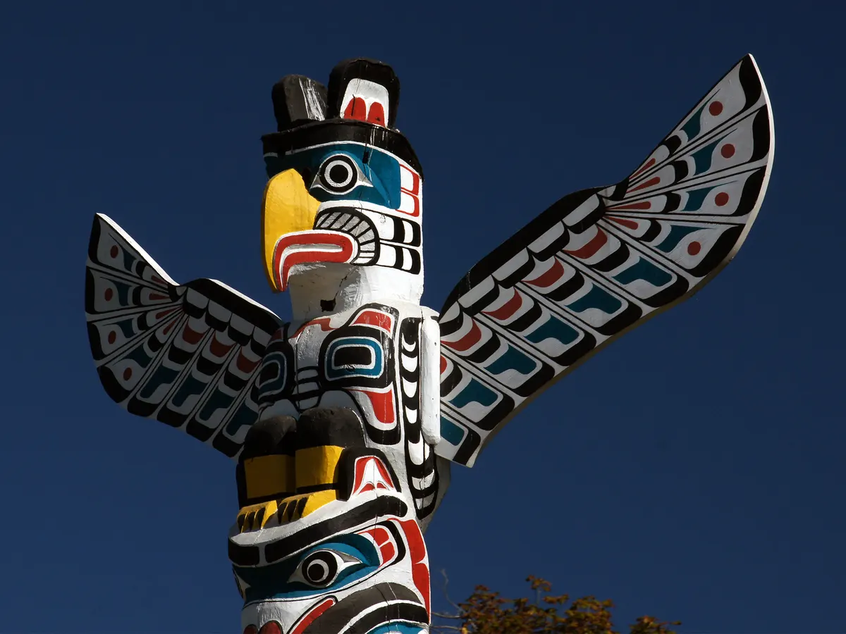 A carved Thunderbird totem pole at Brockton Point against a deep blue sky