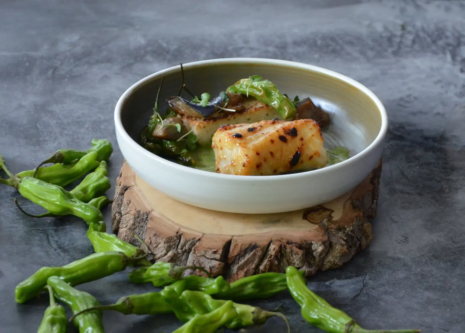 Maple-glazed sablefish plated with grilled shishito peppers and marinated eggplant in cilantro sauce.