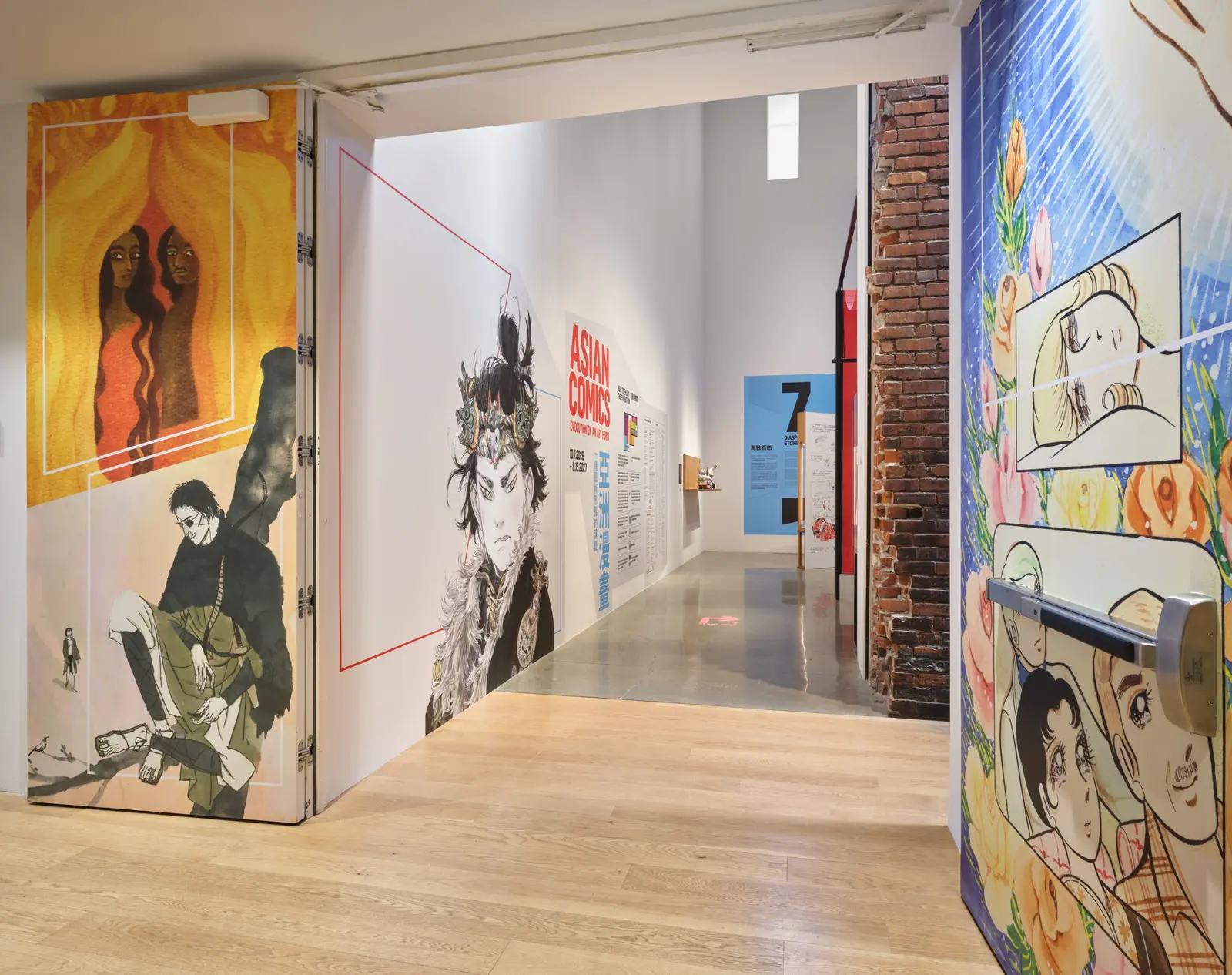 Gallery entrance with large comic-art panels on the walls, including a hooded figure on the left and a colourful manga-style illustration on the right