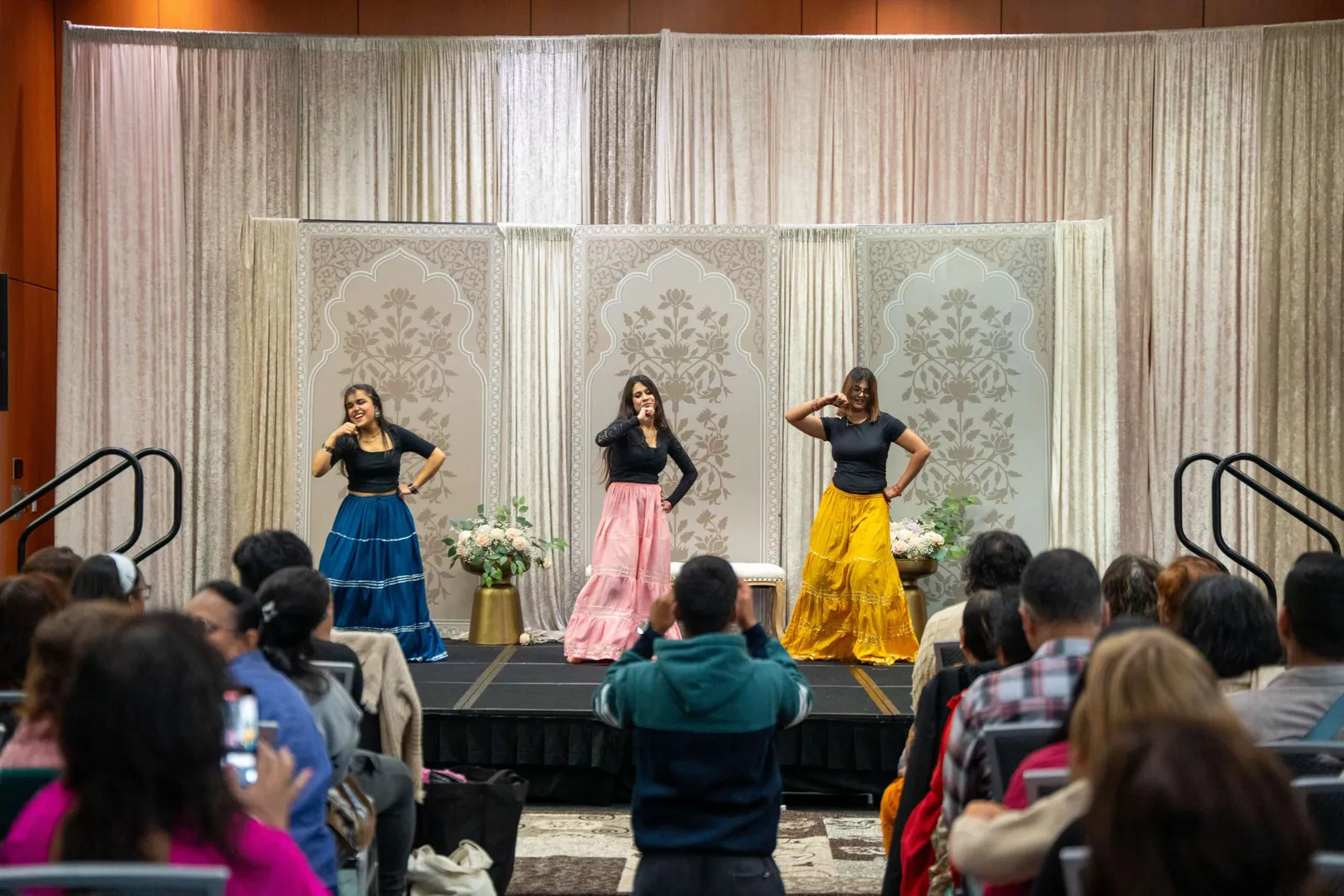 Three dancers in blue, pink and yellow skirts perform for a seated audience at a previous Diwali Fest celebration