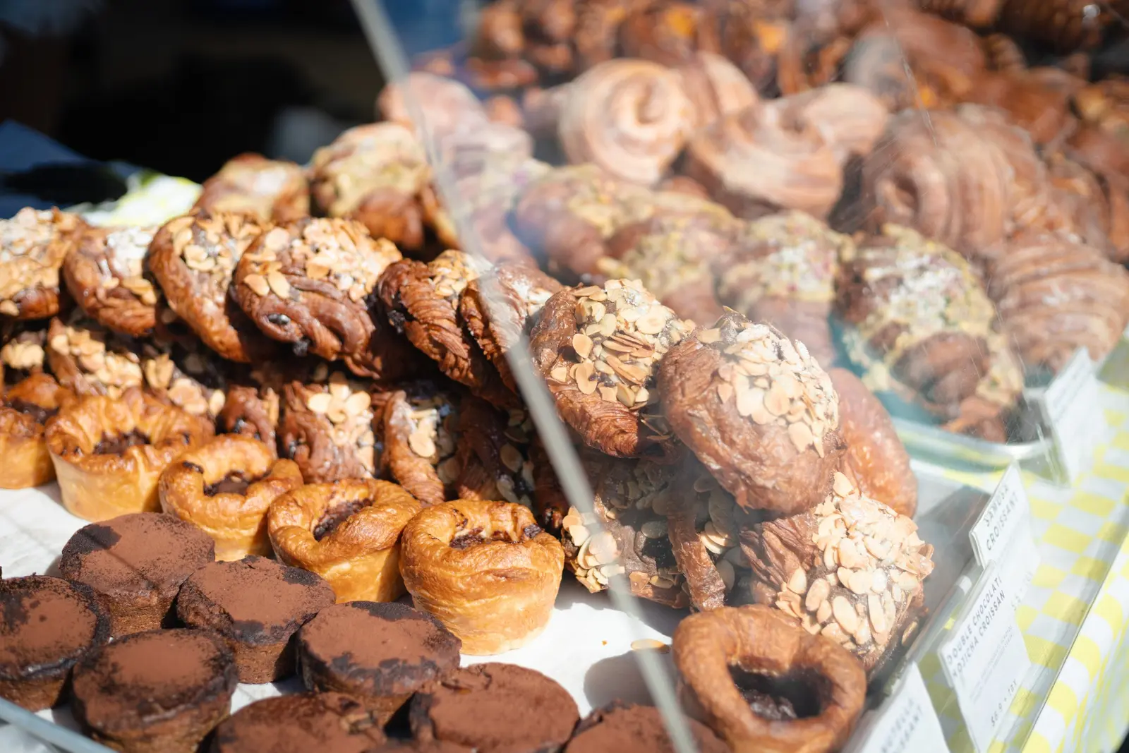 A glass front display case filled with assorted pastries, including chocolate pastries, spiral pastries, and nut-topped baked goods, at Elaichi Patisserie
