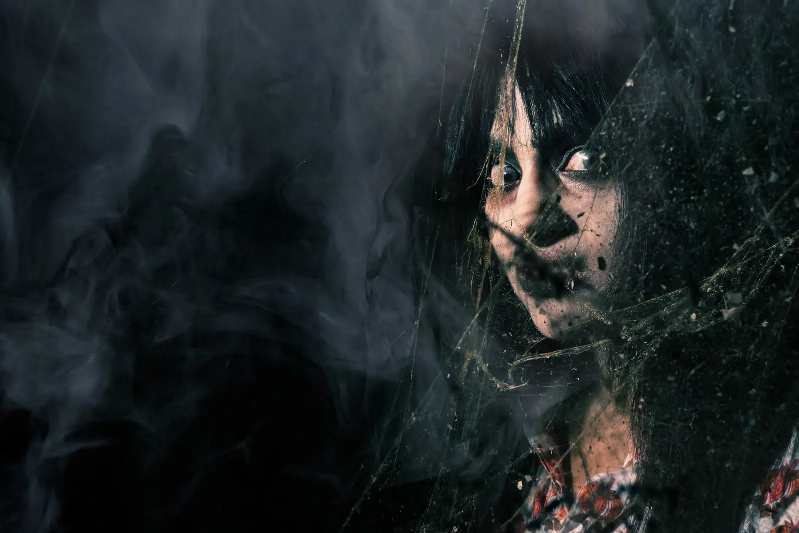 A costumed haunted-attraction performer with long dark hair peers through smoky darkness at Fright Nights.