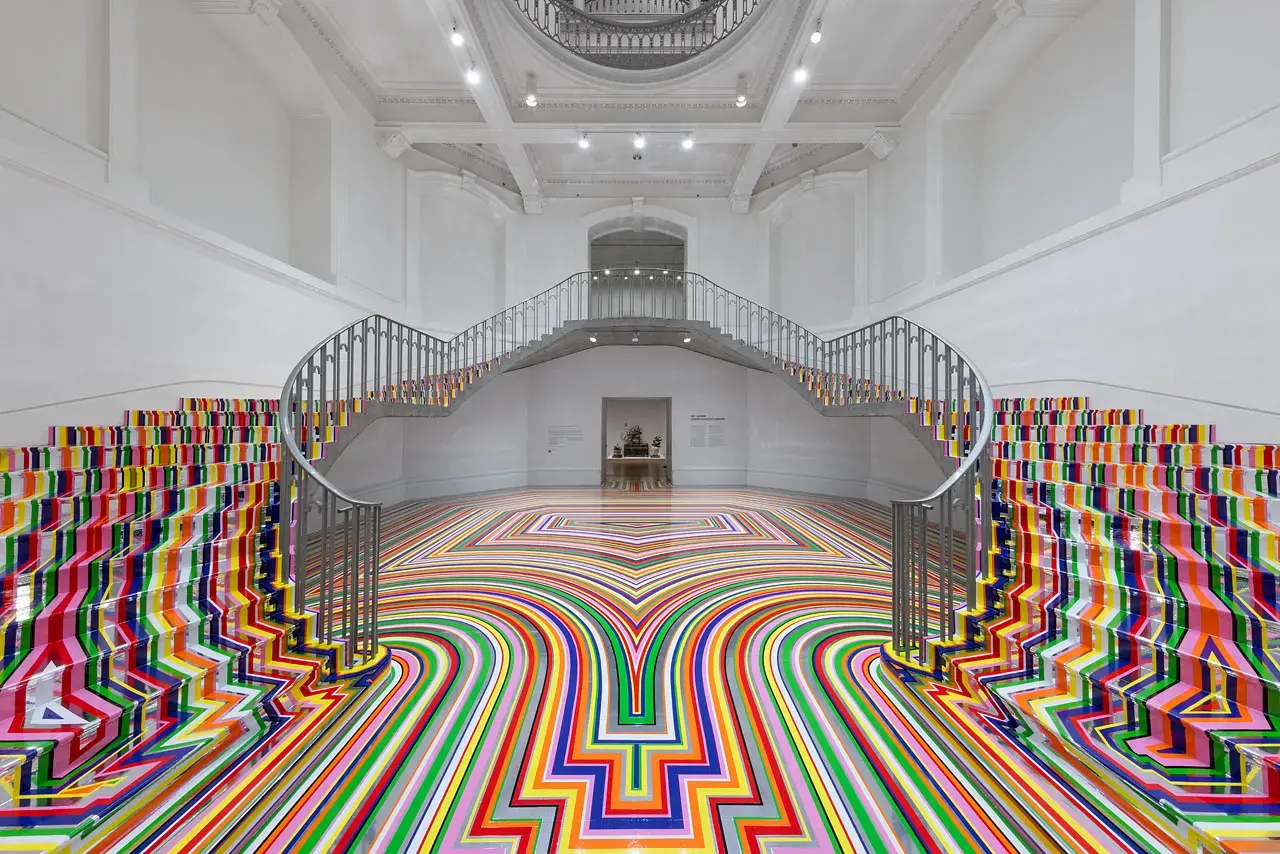Colourful striped floor installation by Jim Lambie wrapping around a staircase in a white gallery room at the Vancouver Art Gallery