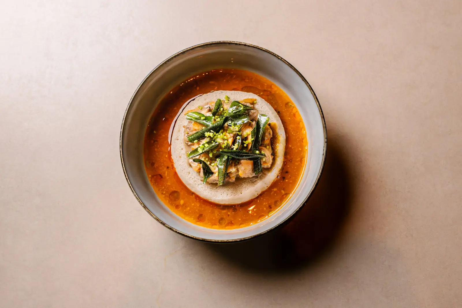 A bowl of food, a soup or curry dish with greens, served on a pale plate.