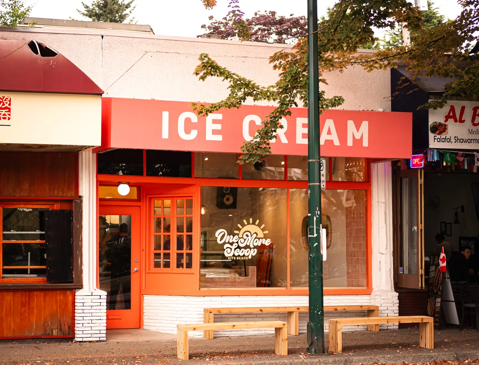 Storefront of One More Scoop ice cream shop with a red-and-white ICE CREAM sign, orange entrance and benches out front