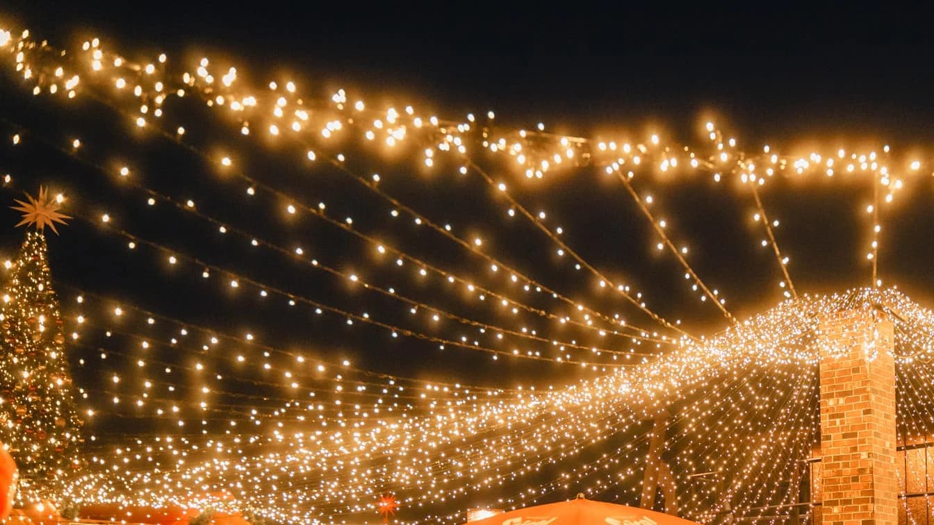 A canopy of warm string lights over the Vancouver Christmas Market at Jack Poole Plaza during the 2025 season, cropped from the market's own photo