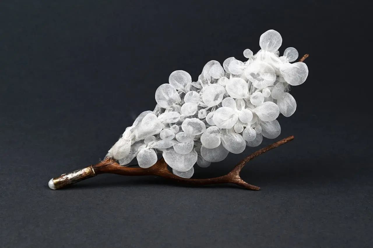 A pale, translucent clustered sculpture mounted on a branching copper-toned form, displayed against a dark background
