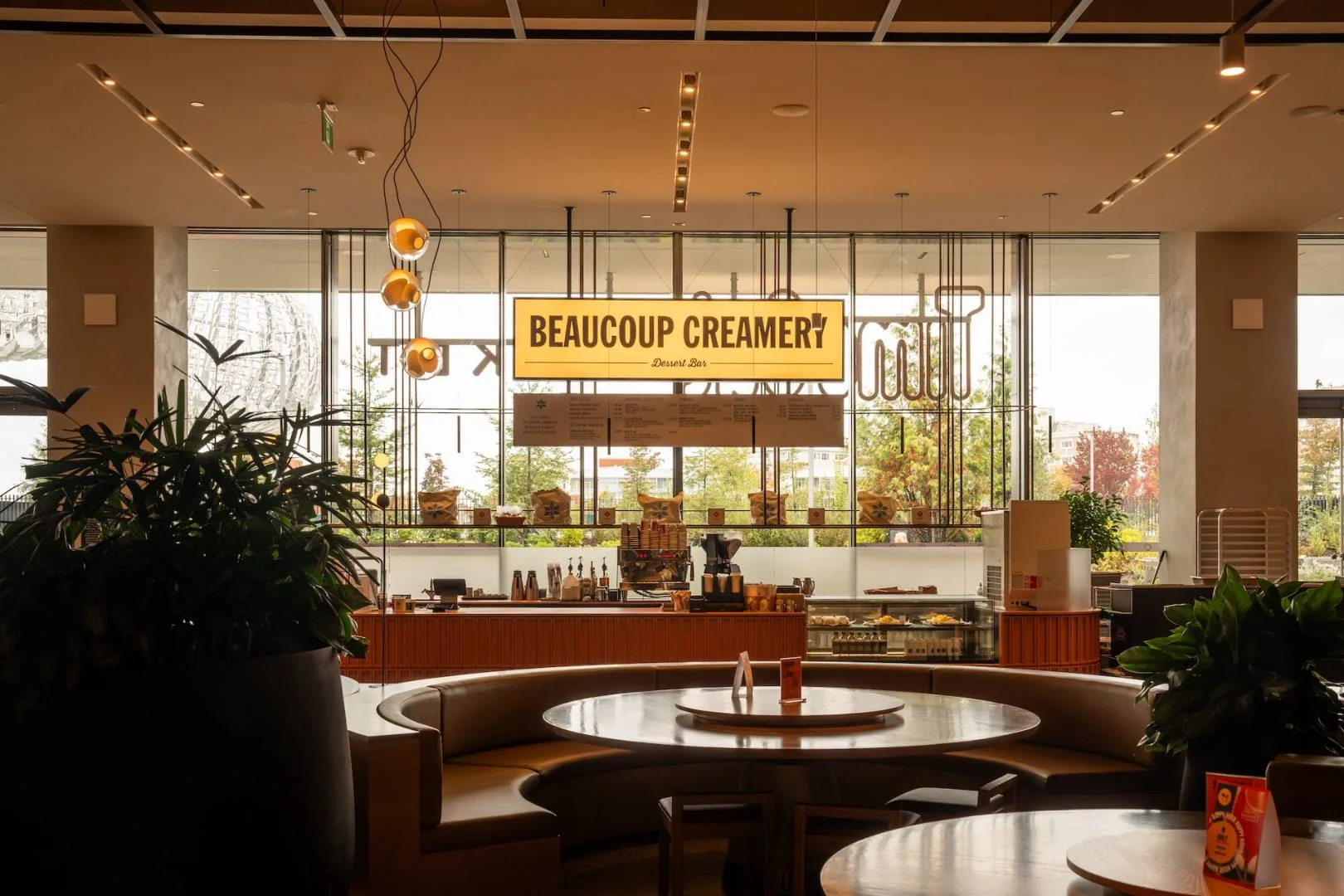The Beaucoup Creamery dessert bar sign and counter at Time Out Market Vancouver, seen past a curved booth and round table
