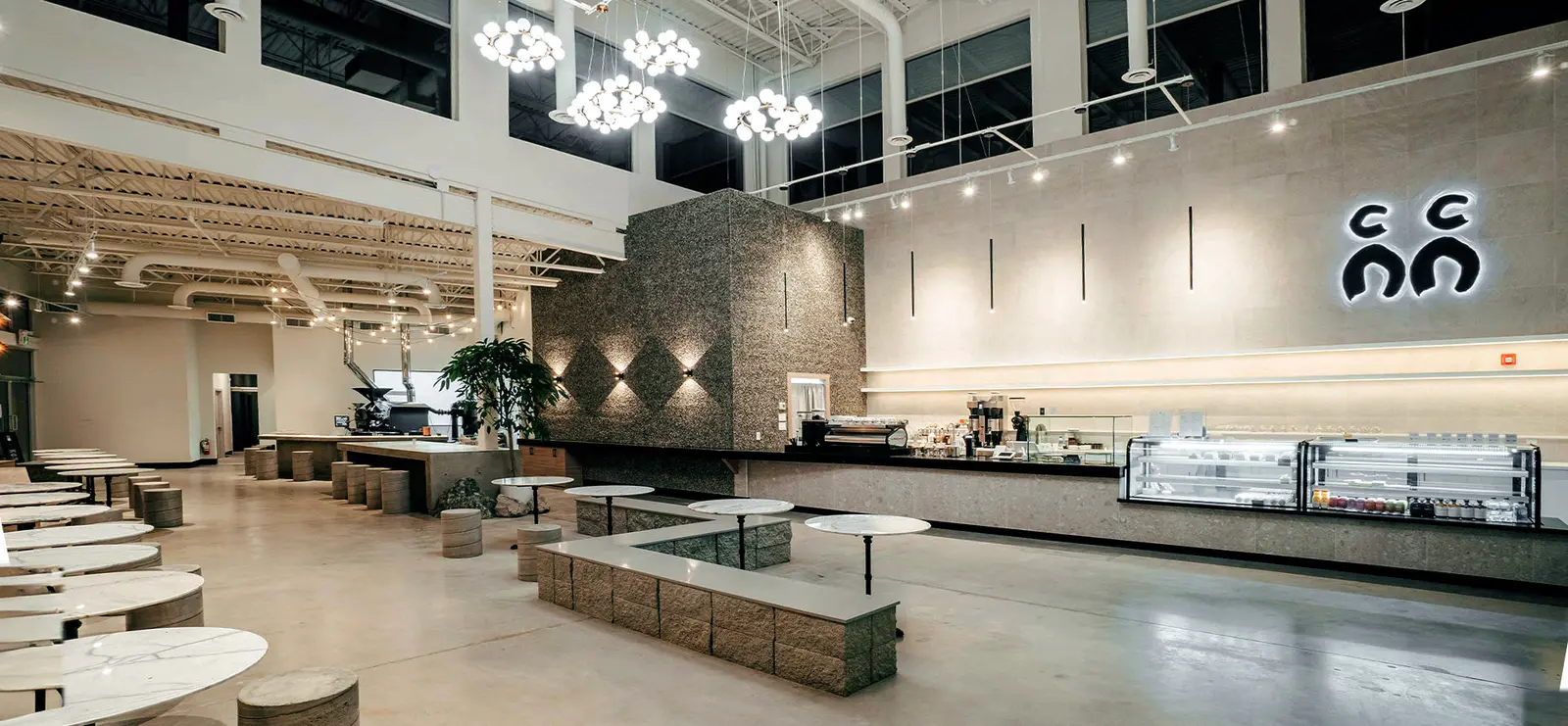 Bright modern C Market Coffee interior with white tables, pendant lights and a long service counter, shown at an existing location rather than the unopened downtown site