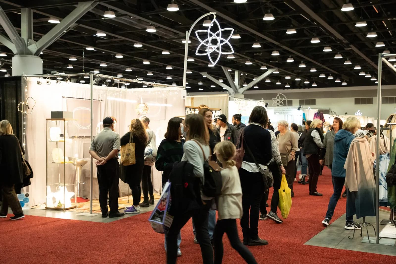 Shoppers walk a red-carpeted aisle between artisan booths under a lit star decoration at an earlier Circle Craft Holiday Market