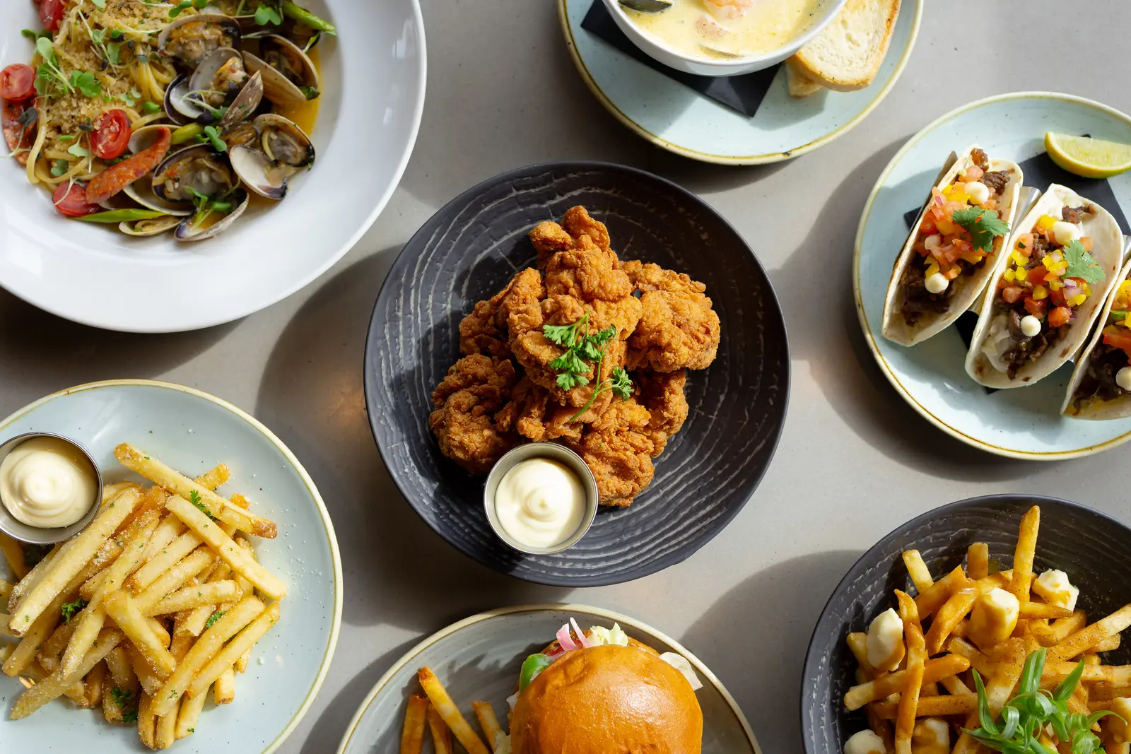A table spread of seafood pasta, fried chicken, tacos, a burger and fries from Papi's Seafood and Oyster Bar, one of the Dine on Denman restaurants