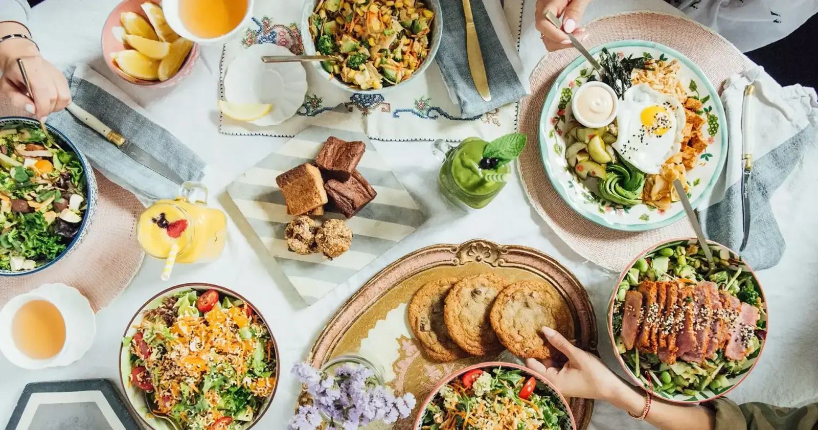 Overhead shot of a table spread with Mandy's salads, smoothies, cookies and baked goods, a brand photograph rather than the Kitsilano interior