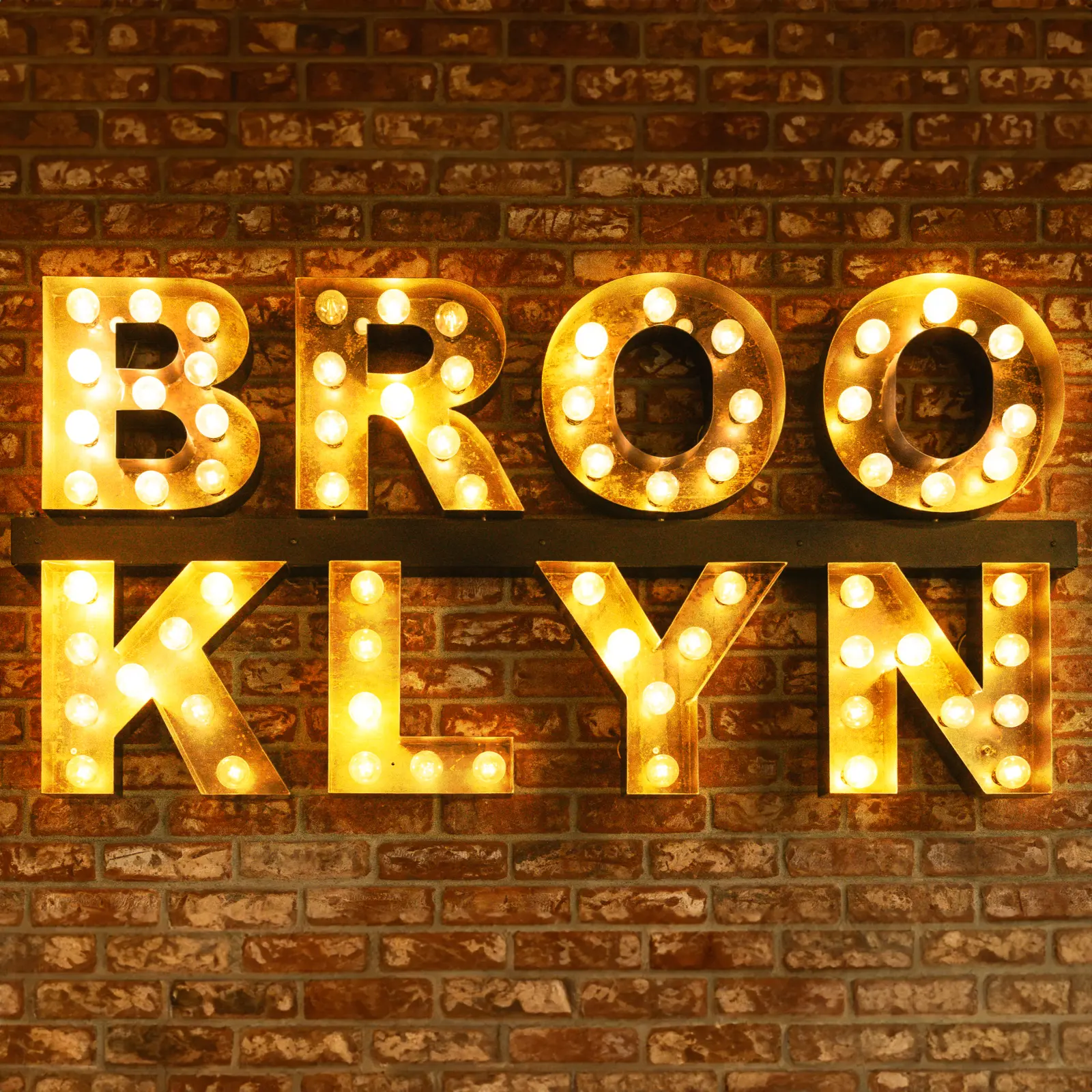 Illuminated marquee sign reading BROOKLYN mounted on a brick wall at Straight Outta Brooklyn Pizza