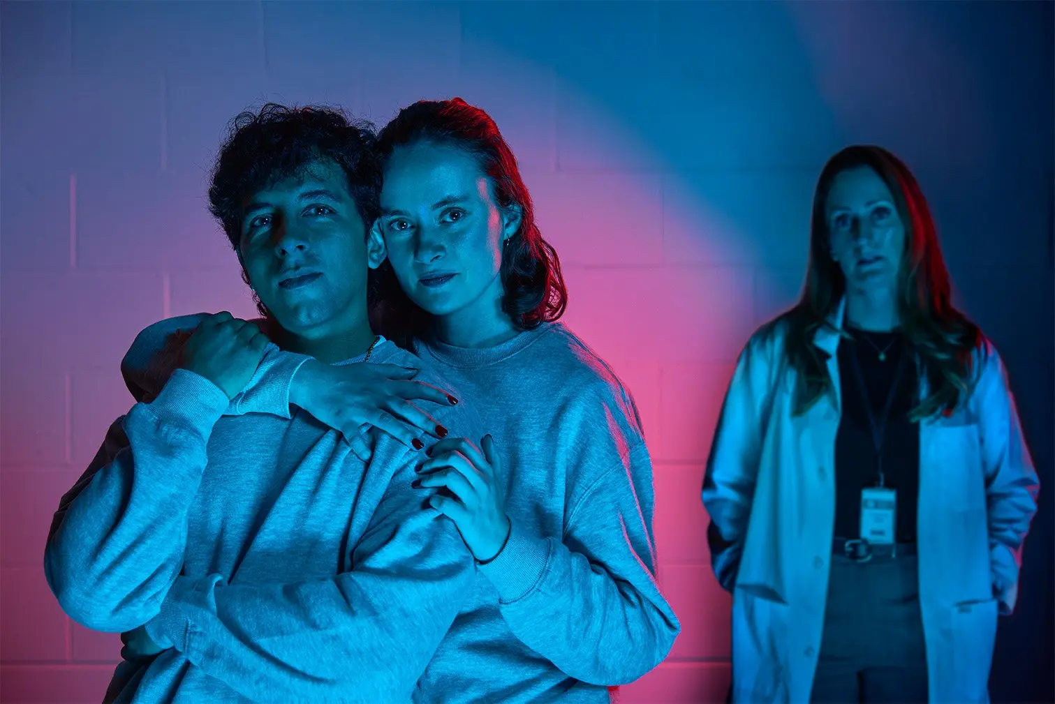 Actors Paige Louter, Andy Kalirai and Meghan Gardiner performing a scene from The Effect under blue and pink stage lighting.