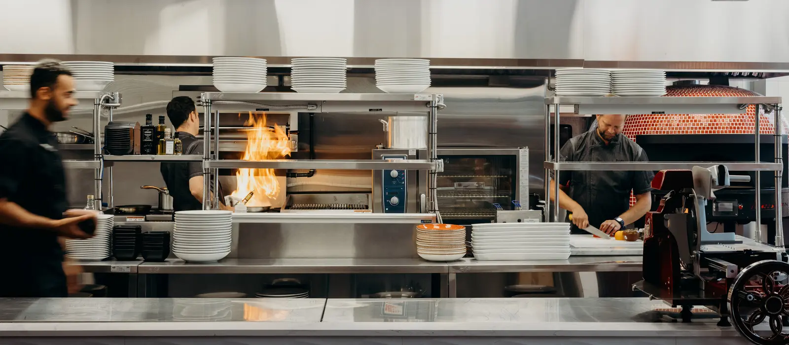 Open kitchen at Tutto Restaurant with staff working behind the counter and flames visible in the oven