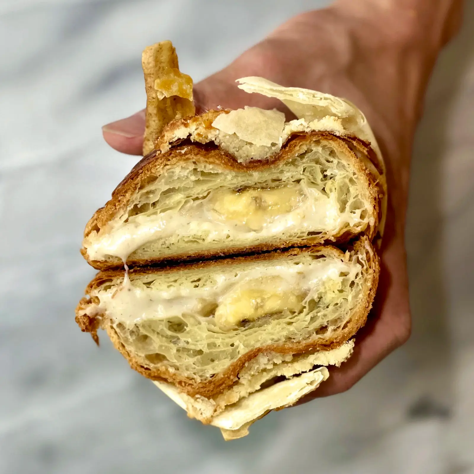 Croissant cut in half, held in hand, showing laminated layers and filling.