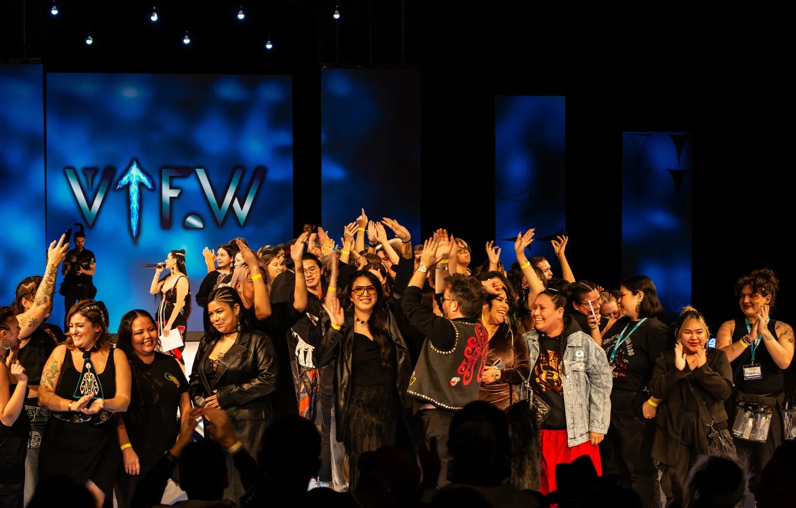 Designers, models and crew celebrate together on stage beneath the VIFW logo at an earlier Vancouver Indigenous Fashion Week finale