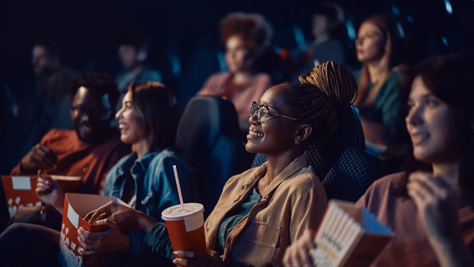 Audience members watching a film in a cinema, holding popcorn and drinks, smiling at the screen